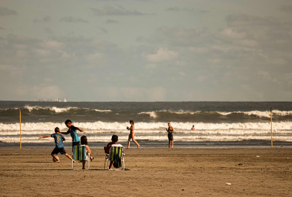 Adults and children having fun on a sandy beach with ocean waves in the background.