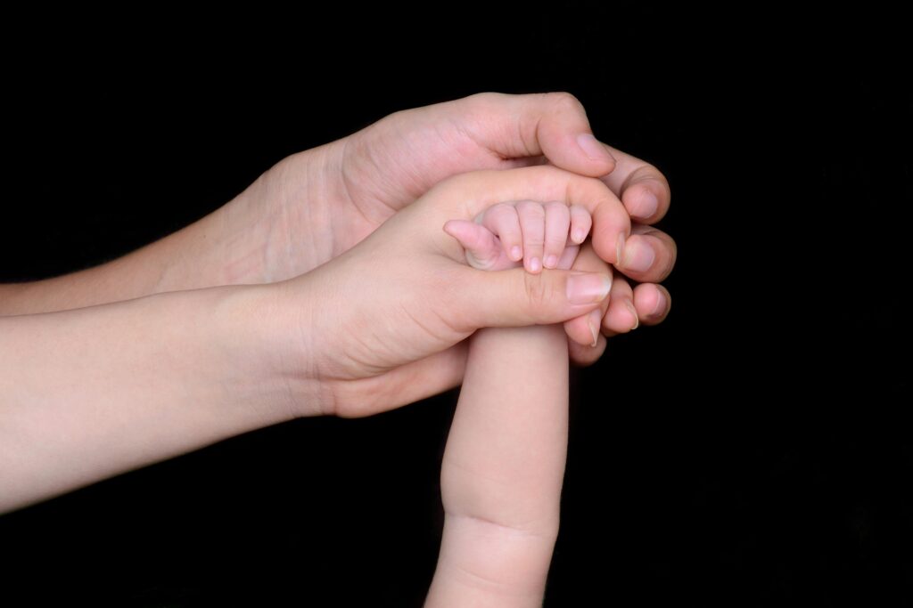 A close-up image featuring a baby's hand being held by a parent's hand, symbolizing love and protection.