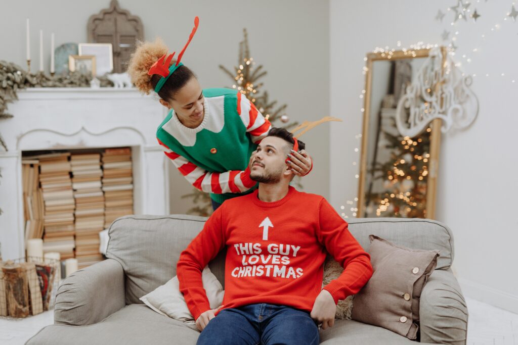 A joyful couple in colorful Christmas sweaters celebrating indoors, capturing holiday spirit.