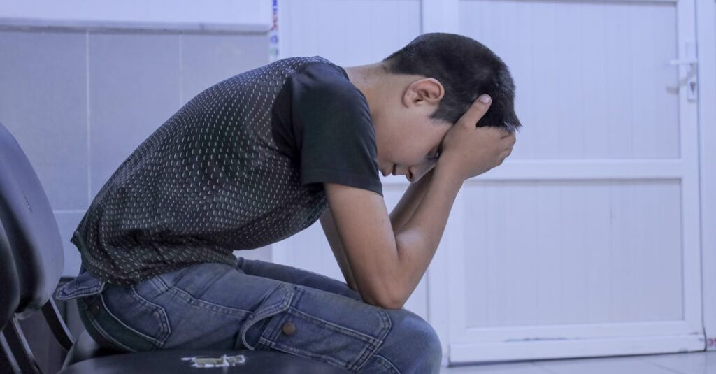 A young boy shows distress while sitting alone in a hospital waiting room, head in hands, conveying emotions of anxiety and sadness.