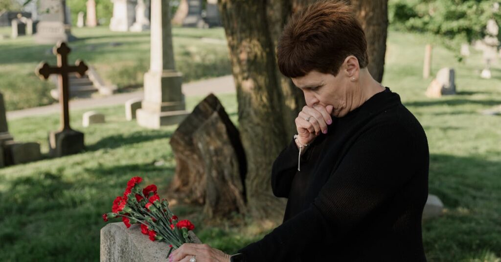 Senior woman in black at a cemetery, grieving by a gravestone with red flowers.
